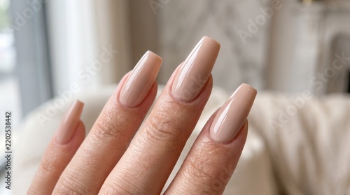 Manicured hands showcasing elegant nude acrylic coffin nails with a glossy finish, highlighting professional nail care and modern cosmetic beauty standards.
