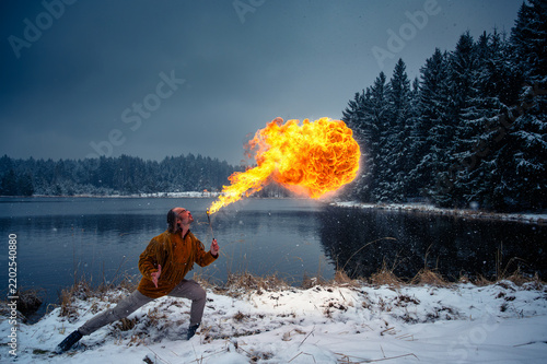 Fotografie Fire breather spitting a huge fireball outdoors on a snowy winter lake shore wit