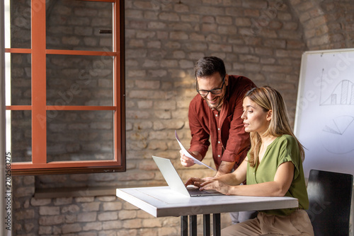Male and female corporate colleagues collaborating, reviewing project data, and typing on a computer screen in a modern workplace