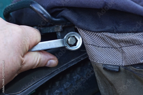 one mans hand with wrench tightening nut on black sports bike on summer street