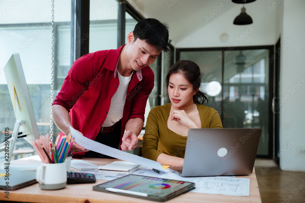 Obraz premium Asian architects collaborating on a residential design project, reviewing blueprints, color palettes, and architectural plans while working on a laptop in a modern studio.