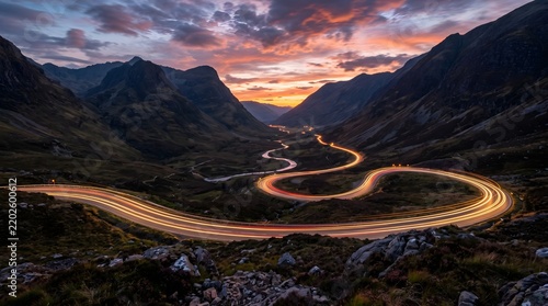 Cinematic mountain pass at sunset with winding road light trails, dramatic highland valley landscape, long exposure car lights on curvy highway