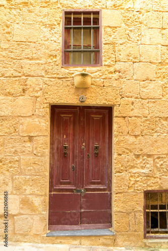 Traditional burgundy wooden door set in a historic limestone facade in the medieval city of Mdina.