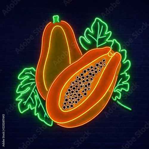 Bright neon sign depicting sliced papaya fruit with leaves against dark brick wall