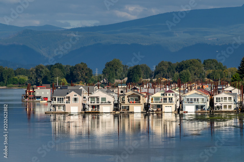 View of floating houses on the Columbia River with reflections in the water and mountains in the background in Portland, Oregon, United States.