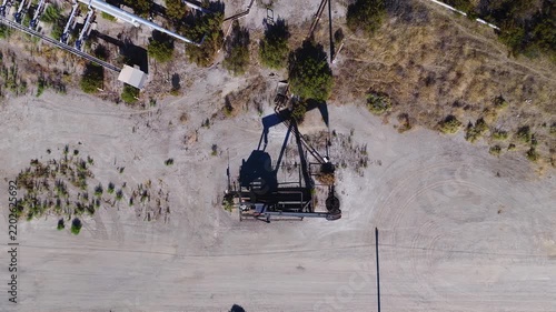 Aerial top down perspective shows an operating oil pump jack working on arid ground in California, USA. Oil tariffs, trade war, price plunge.