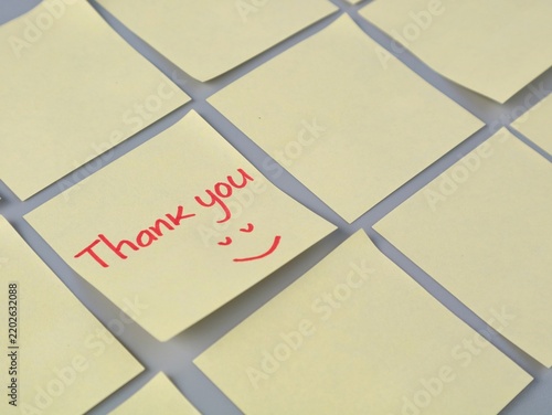 Obraz na plátně Close up of a yellow adhesive note with a handwritten Thank you message and happy face in red ink, surrounded by blankadhesive notes on a flat surface
