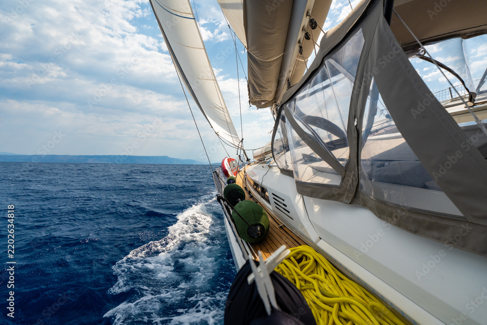 Obraz premium Dynamic view from deck of sailing yacht heeling under wind power while cutting through Adriatic waters. White wake, filled sails, a sense of speed, freedom and offshore adventure