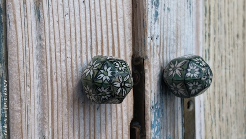 Close-up of an old weathered wooden door featuring two ornate floral ceramic door handles