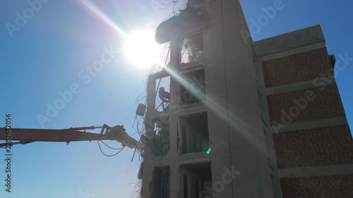 A crane demolishing a multi-story building in sunny weather.