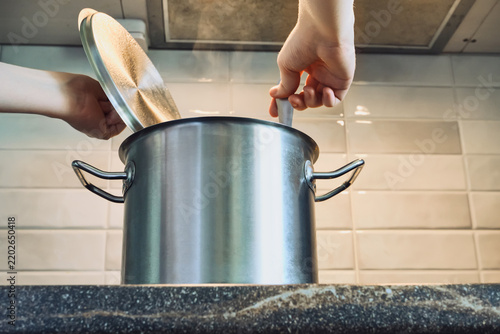 Fotografie Person stirring broth in steaming pot on kitchen countertop