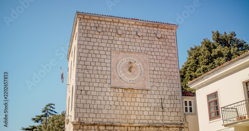 Krk, Croatia - 19 September 2026: View of the historic stone clock tower in the old town of Krk, featuring detailed masonry and a clear blue sky.