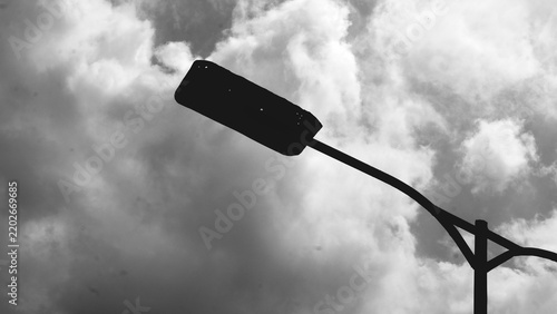Quadro su tela Black and white silhouette of a street lamp against dramatic clouds, creating a high contrast urban scene with atmospheric sky and minimalist composition