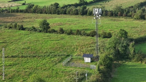 An aerial view of a telecommunications tower equipped with solar panels in a lush green field, representing sustainable technology and remote connectivity.