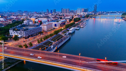 Photography Bridge traffic above moored riverboats and a city waterfront