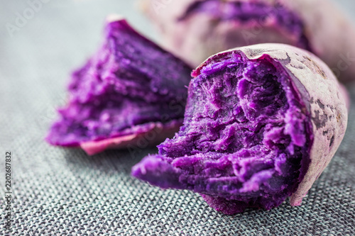 Cooked purple sweet potatoes with vivid deep purple flesh, presented on a textured gray surface as ready-to-eat food.