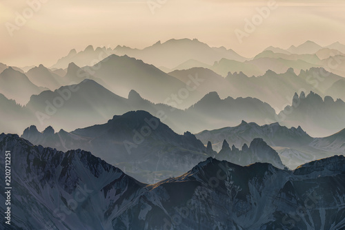 Endless ridgelines dissolve one behind another into soft cream mist in a minimalist dawn mountain panorama