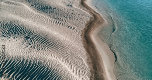 Textured sand ripples meet clear turquoise water at the ocean's edge