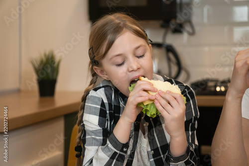 Obraz na płótnie Girl with blonde braids wearing a plaid shirt enjoying a fresh sandwich at a kit