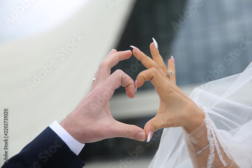 with the bride's finger resting her delicate diamond engagement ring and manicured nails on the cover, and the groom's on his suit sleeve, forming a heart shape with the bride . Heart-shaped hands,