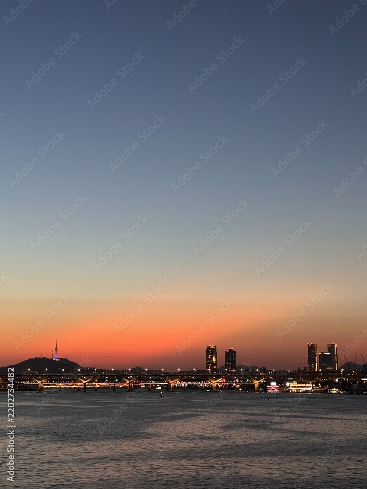 Fototapeta premium Vertical view of Seoul skyline and N Seoul Tower during vibrant orange sunset over Han River