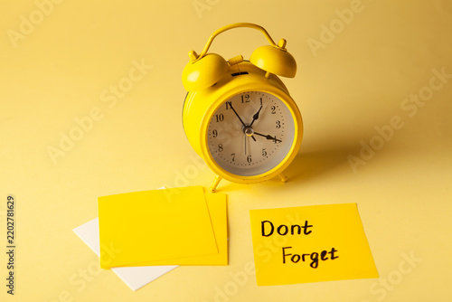 Fotografie Yellow alarm clock and yellow sticky notes with text Don't forget on yellow back