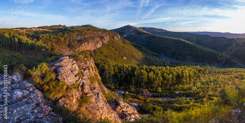 A sunlit rocky cliff overlooks a sweeping landscape