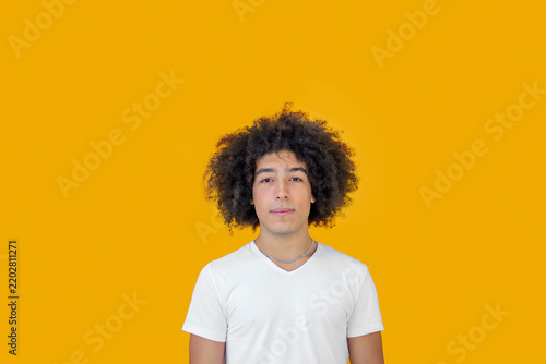 Portrait beautiful men of mixed race african-Italian on a yellow background. A young ethnic man with curly hair in a white t-shirt looks positive, relaxed 