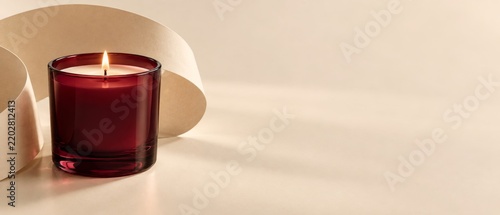 Lit red candle in glass jar on cream backdrop. Minimalist product banner. Cream and garnet red color palette.
