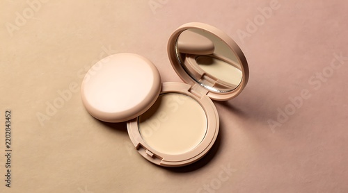 Open and closed makeup compact powder with mirror on a soft peach background, cosmetic face foundation for skin tone correction and beauty routine, professional makeup product photography.
