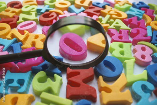 Magnifying glass focuses on a pink number zero among scattered colorful alphabet and number letters.