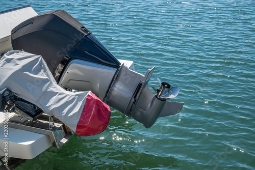 Close view of a raised outboard boat engine with exposed propeller above water at a marina.