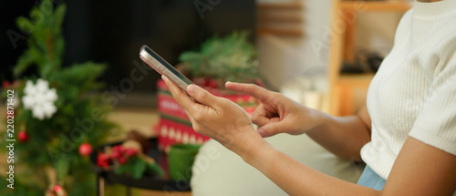 Young woman using mobile phone for Christmas celebration. Close-up of female hands holding smartphone for online message, holiday shopping, xmas festive greetings. Side view