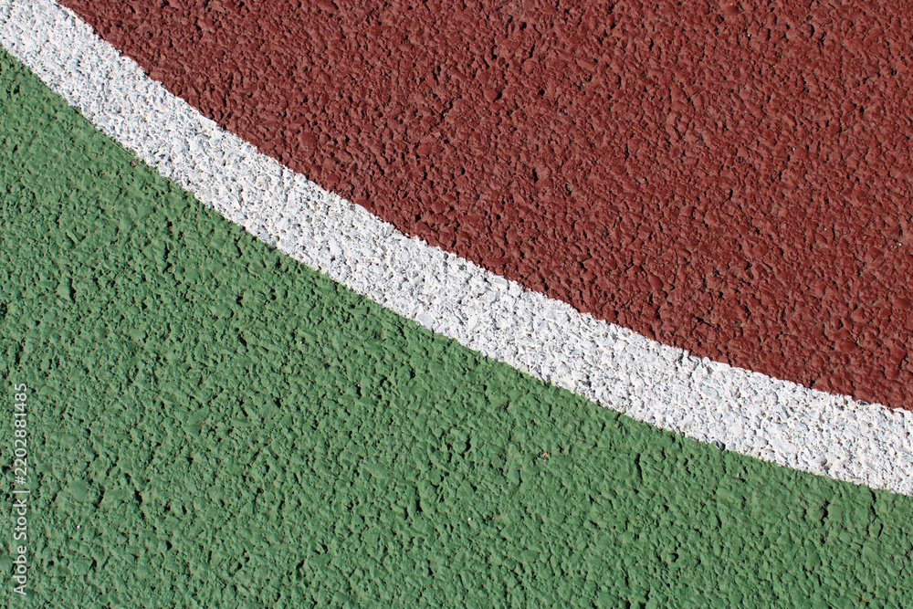 Obraz premium Gros plan sur les lignes de marquage blanches d'un terrain de sport extérieur en revêtement synthétique vert et rouge bordeaux.
