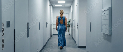 Woman in blue dress walking down long white hallway corridor