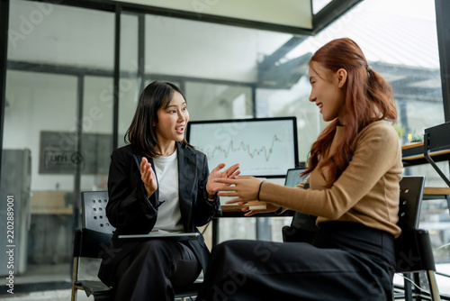 Two Asian businesswomen collaborating, discussing financial data and investment growth during a professional office meeting, showing teamwork and planning