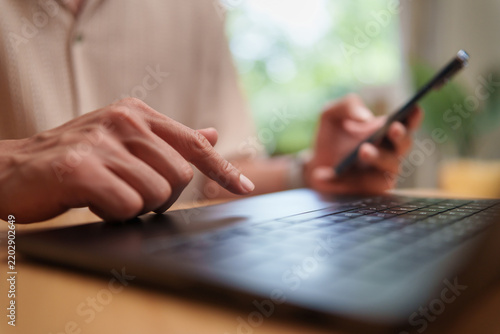 Asian Man browsing with a smartphone and laptop at home, representing online digital communication, technology and modern lifestyle.