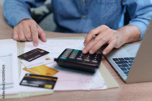 Man calculating bills and credit card payments beside a laptop at home, representing debt management, personal finance, monthly expenses, budgeting, borrowing and financial responsibility.