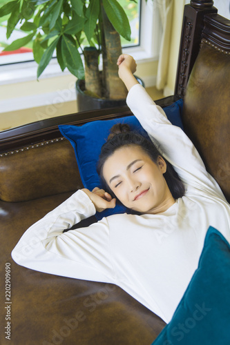Obraz na płótnie Relaxed young woman resting on a leather sofa with eyes closed in a cozy living