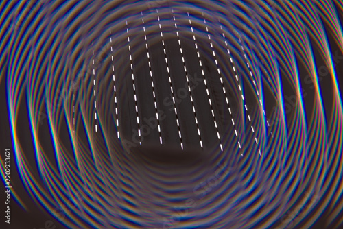 Abstrakte Nahaufnahme mit kreisförmigen Linien, Lichtbrechungen und wiederholten geometrischen Strukturen. Der optische Effekt erzeugt eine tunnelartige Perspektive