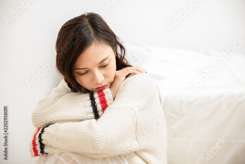 Foto Sad young woman sitting on bed at home hugging herself in deep thought