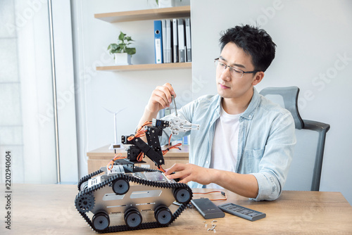 Young engineer repairing a tracked robot on a desk in a modern office