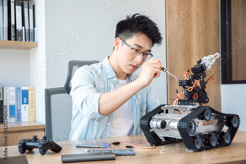 Young engineer repairing a tracked robot with a screwdriver at a desk in a home office