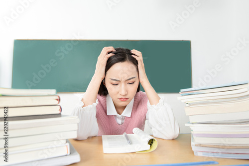 Stressed student studying with piles of books in a classroom