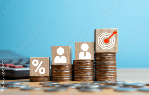 Wooden blocks with percentage, human resources, and target icons on increasing coin stacks for business growth and financial goals on blue background