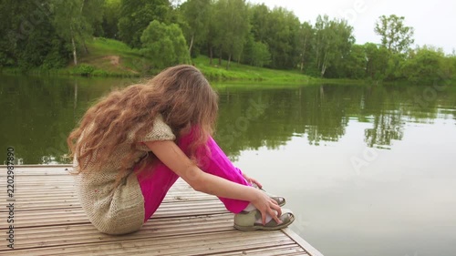 little sad girl is sitting on bridge near lake