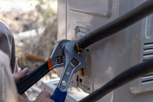 Close-up of a technician tightening a brass nut on a copper pipe with adjustable wrenches during air conditioner installation. Professional HVAC service, maintenance and split system connection