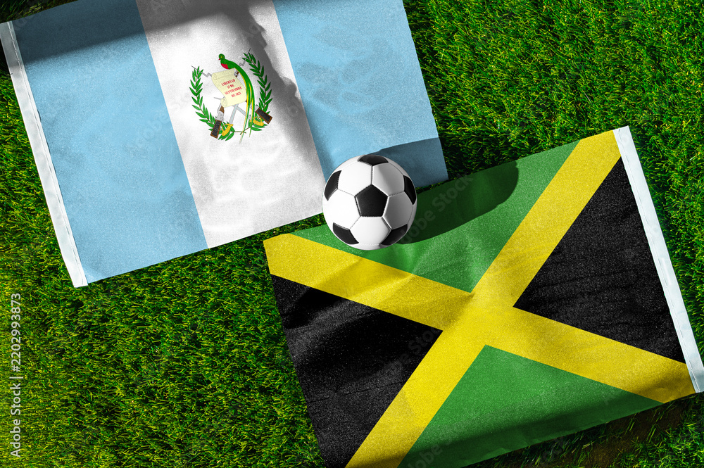 Fototapeta premium Guatemala vs. Jamaica football match. National flags on green grass with soccer ball in the middle. Football background for international match.