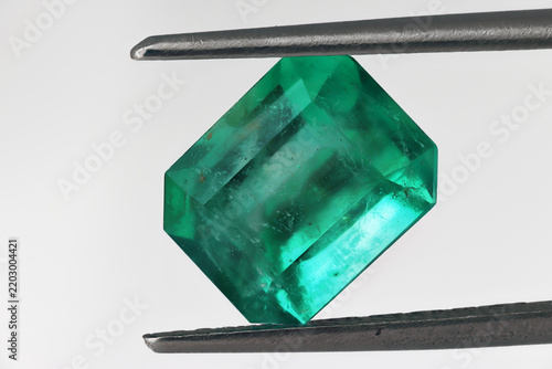 Colombian emerald cut green gemstone held in tweezers, close-up macro on white background