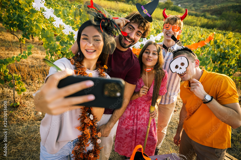 Obraz premium Group of cheerful friends taking a selfie at an outdoor Halloween party in a vineyard.